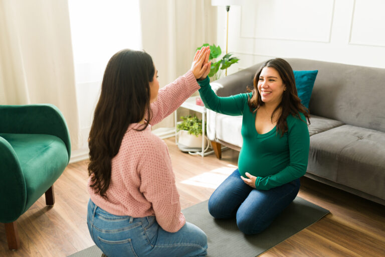 Happy doula and pregnant woman sharing a joyful high five during a supportive home visit, celebrating connection and trust in motherhood