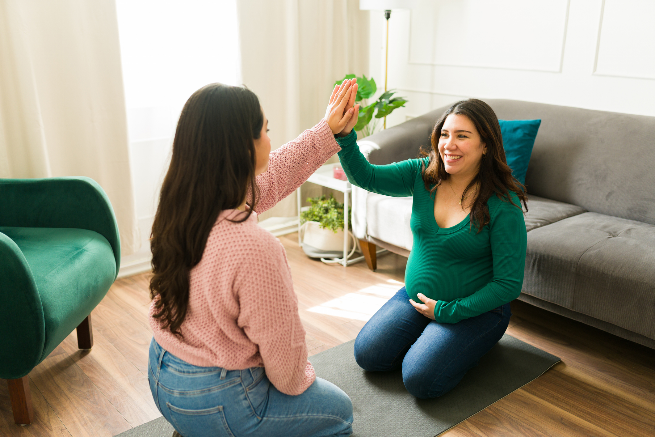 Happy doula and pregnant woman sharing a joyful high five during a supportive home visit, celebrating connection and trust in motherhood