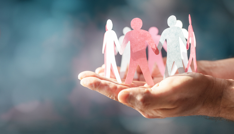 Hands cupping a circle of pink, white, and blue paper figures symbolizing unity and support.