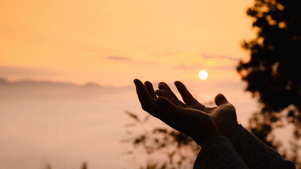 Silhouette of woman praying at sunrise, embracing faith amid summer sky and nature’s beauty.