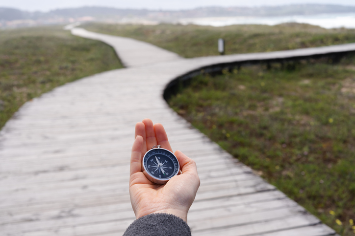 A person holding a compass on a wooden boardwalk. The promenade has two paths.