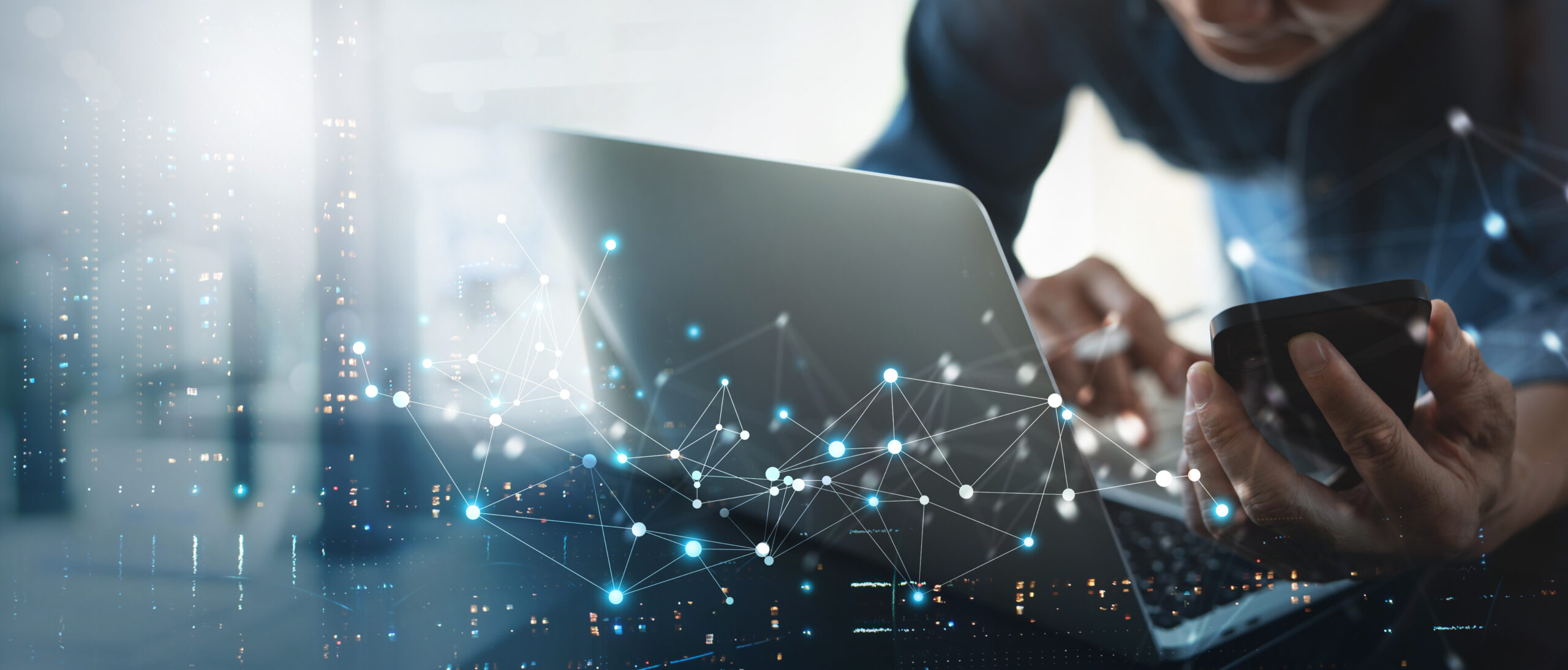 Close-up of a person working on a laptop while holding a smartphone, with a visual overlay of connected nodes and lines symbolizing digital networks and data flow.