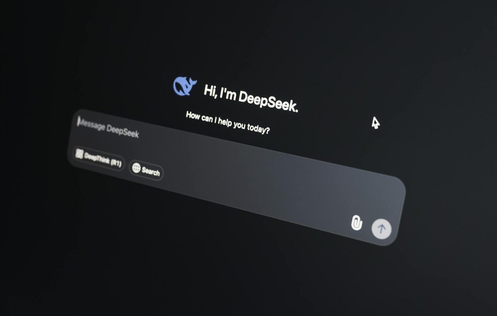 Close-up photograph of a laptop screen in a dark environment displaying the DeepSeek AI chat interface. The screen shows the DeepSeek logo and the text 'Hi, I'm DeepSeek. How can I help you today?' with an empty message input field. The laptop keyboard is partially visible in the foreground.