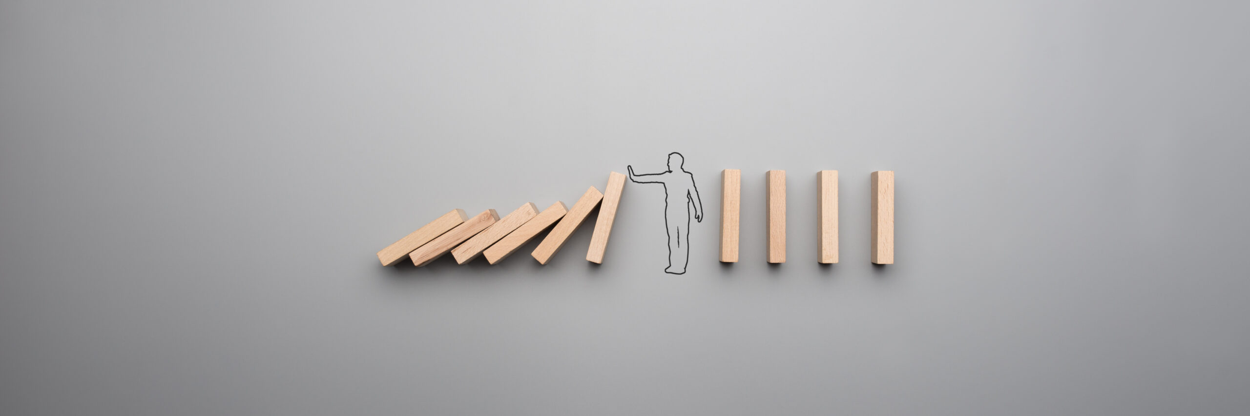 Hand-drawn figure stopping a falling domino while upright dominoes remain standing.
