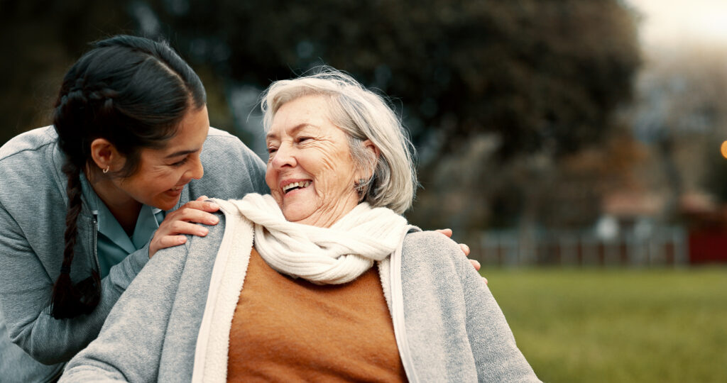 Nurse talking to happy senior patient in wheelchair for rehabilitation, therapy and conversation in garden.