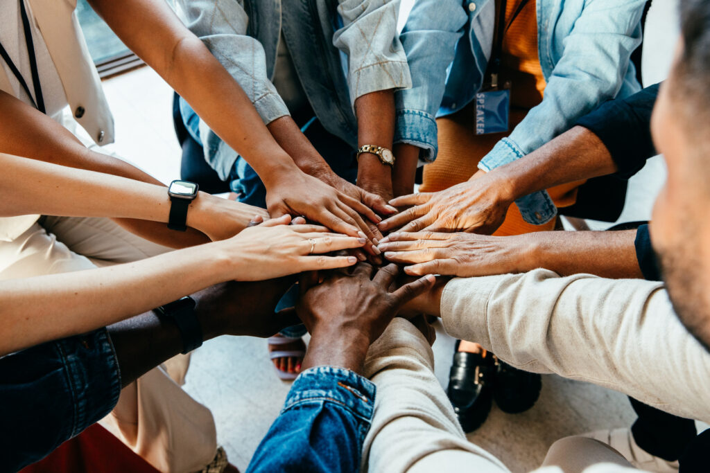 Group of people stacking hands together in a circle during a team meeting or collaboration session.