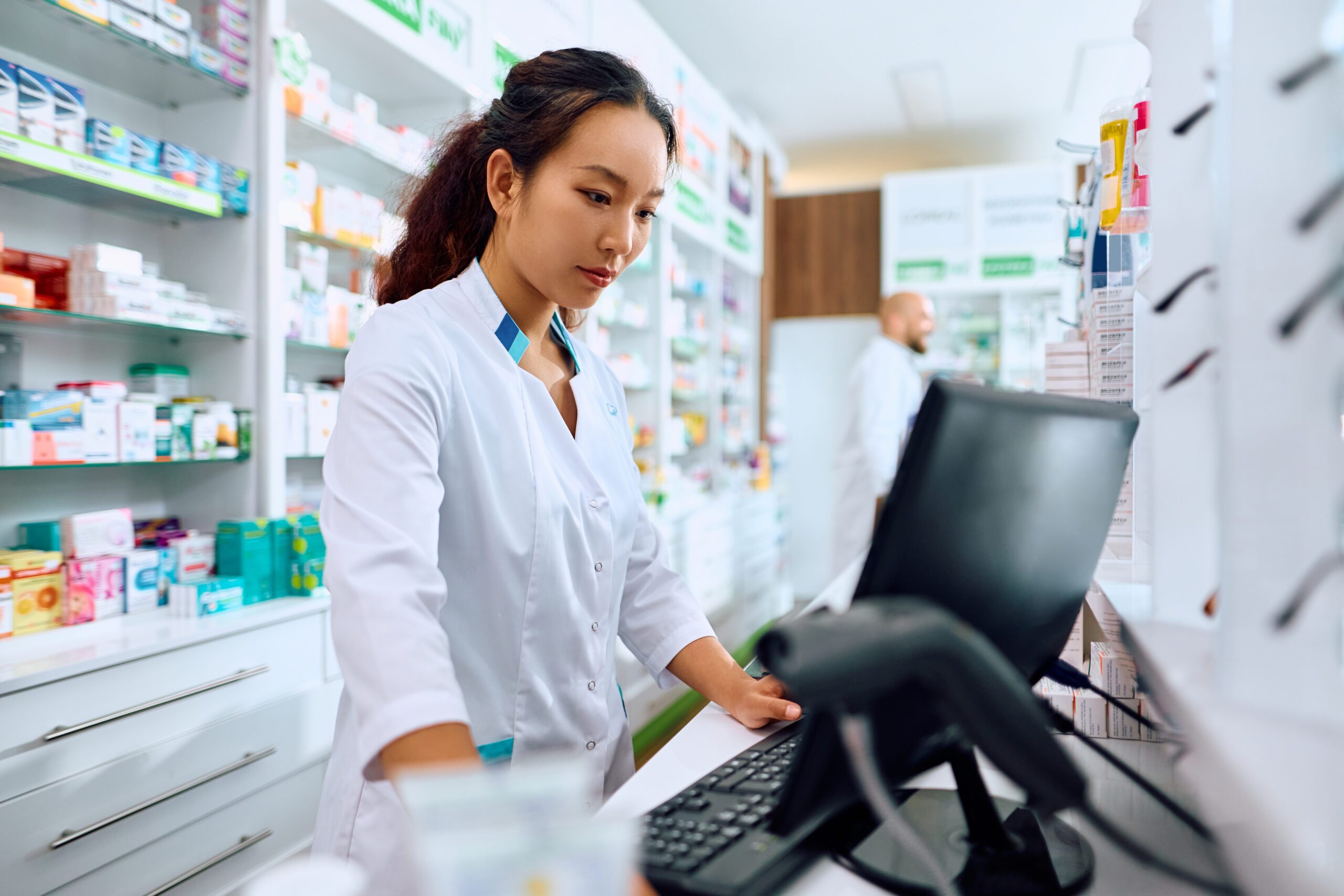 Female Chinese pharmacist using computer while working in a pharmacy.