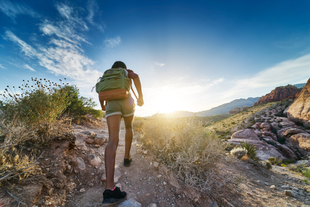 athletic african american woman hiking through red rock canyon in nevada at sunset shot from behind