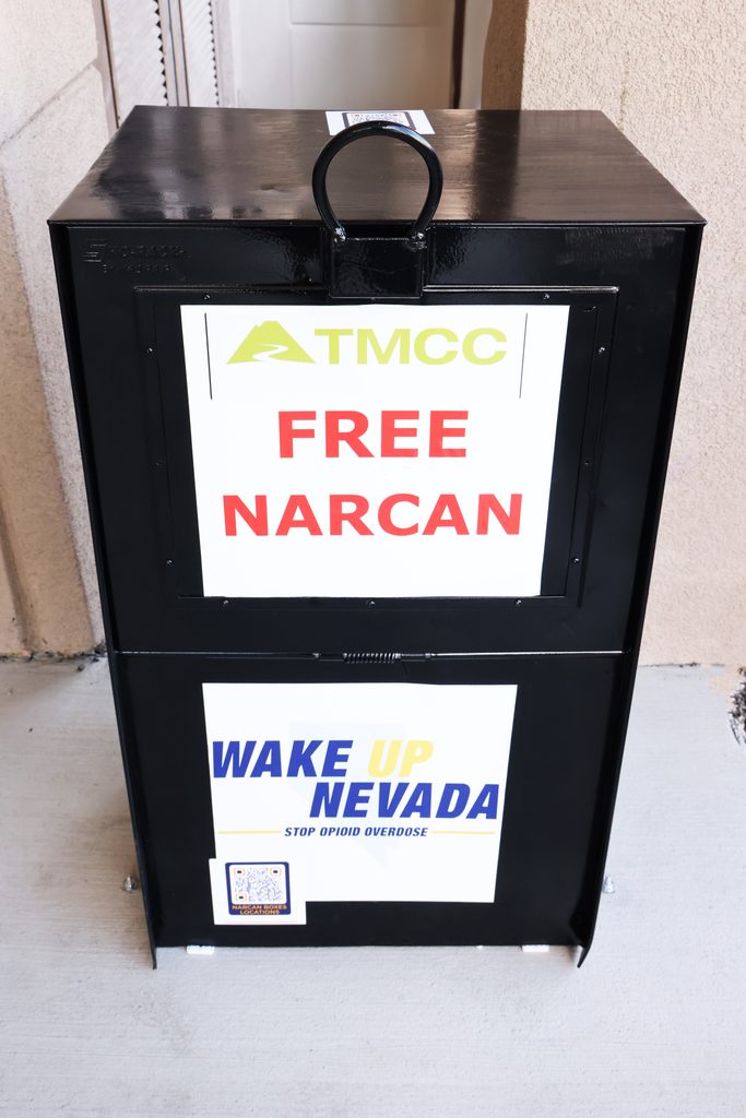 A black box labeled "TMCC FREE NARCAN" and "WAKE UP NEVADA STOP OPIOID OVERDOSE" is placed outdoors to distribute naloxone.