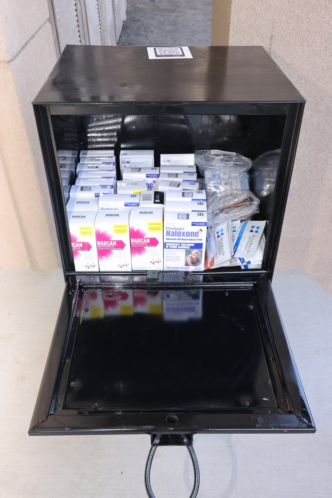 A black, open naloxone distribution box contains multiple boxes of Narcan and Padagis Naloxone, along with other emergency medical supplies.