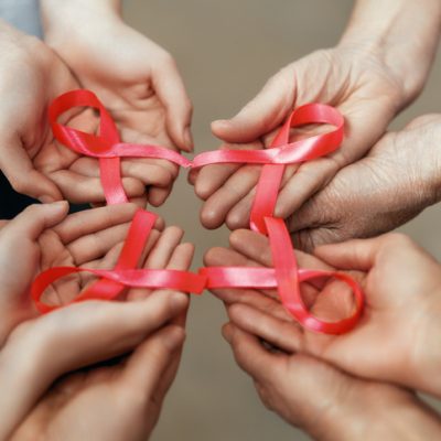 Hands with red satin ribbons symbolizing concept of red ribbon week
