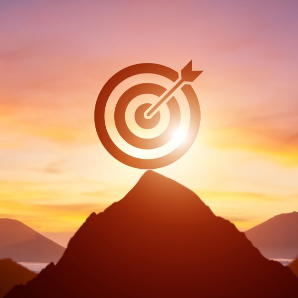 Silhouette target dartboard achievement concept with bullseye on mountain peak at sunrise.