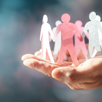 Hands cupping a circle of pink, white, and blue paper figures symbolizing unity and support.